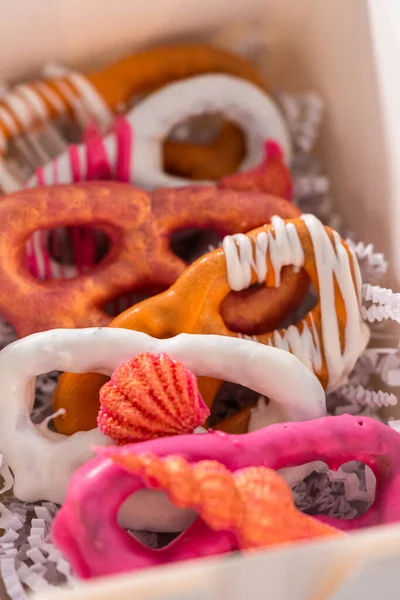 Packaging gourmet chocolate-covered pretzel twists into a white paper gift box filled with paper shreds.