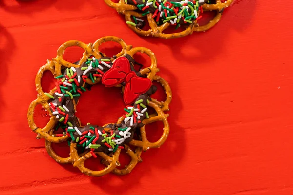 チョコレートプレッツェルクリスマスの花輪は 赤い背景にスプリンクルと赤いチョコレート弓で飾られています — ストック写真