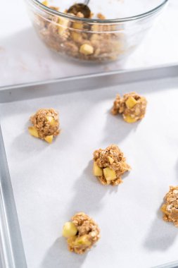 Elmalı yulaflı kurabiye pişirmek için parşömen kağıdıyla kaplı kurabiye tepsisine kurabiye hamuru atmak..