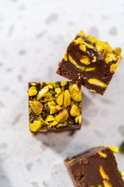 Homemade chocolate pistachio fudge square pieces on a kitchen counter.