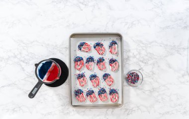 Flat lay. Dipping pretzels twists into melted chocolate to make red, white, and blue chocolate-covered pretzel twists.