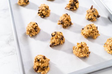 Yumuşak yulaf ezmeli, cevizli, kuru üzümlü kurabiye pişirmek için parşömen kağıdıyla kaplı bir yemek tepsisine hamur kepçesiyle kurabiye pişirmek..