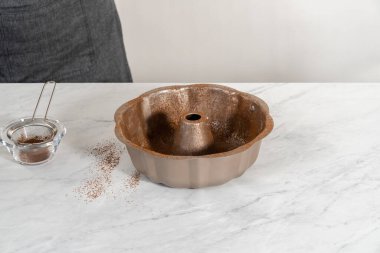 Greasing metal bundt cake pan with vegetable shortening and cocoa powder to bake gingerbread bundt cake with caramel filling.