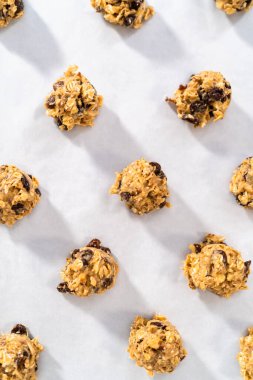 Yumuşak yulaf ezmeli, cevizli, kuru üzümlü kurabiye pişirmek için parşömen kağıdıyla kaplı bir yemek tepsisine hamur kepçesiyle kurabiye pişirmek..