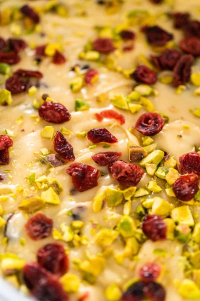 Removing cranberry pistachio fudge from a square cheesecake pan lined with parchment.