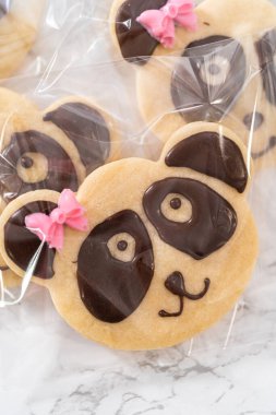 Packaging panda-shaped shortbread cookies with chocolate icing into individual clear bags. clipart