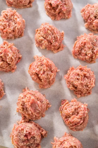 Scooping ground meat with dough scoop into a baking sheet lined with parchment paper to prepare oven-baked meatballs.