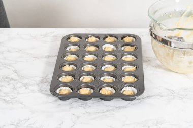 Scooping cupcake batter with dough scoop into a baking pan with liners to bake American flag mini cupcakes.