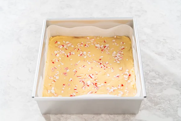 stock image Filling square cheesecake pan lined with parchment paper with fudge mixture to prepare candy cane fudge.