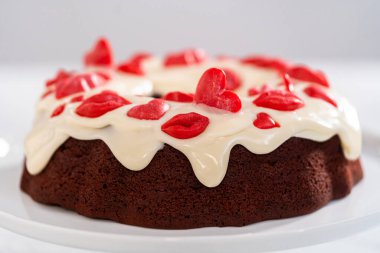 Freshly baked red velvet bundt cake with chocolate lips and hearts over cream cheese glaze for Valentines Day.