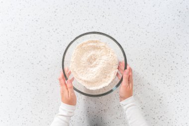 Flat lay. Mixing dry ingredients with a hand whisk in a large glass mixing bowl to bake a simple vanilla bundt cake.