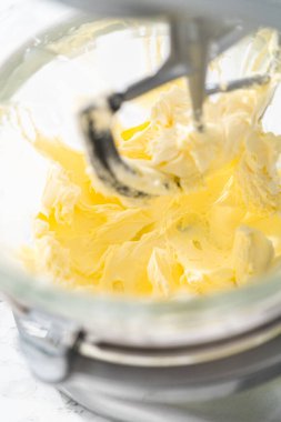 Whisking buttercream frosting in a glass mixing bowl with an electric kitchen mixer for American flag mini cupcakes.