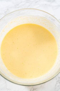 Büyük bir bardakta ıslak malzemeler karıştırarak kırmızı kadife kekler ve beyaz çikolatalı ganache kreması pişiriyorum..