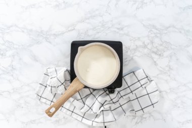 Flat lay. Heating whipped cream in a saucepan to make the white chocolate ganache frosting.