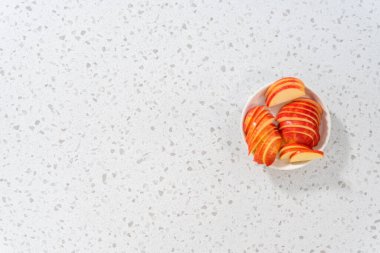 Düz yatıyordu. İnce dilimlenmiş kırmızı elmalar beyaz bir tabakta.