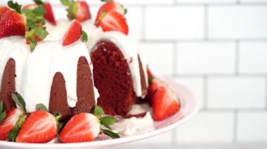 Step by step. Slicing red velvet bundt cake with cream cheese frosting garnished with fresh strawberries.