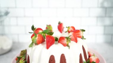 Red velvet bundt cake with cream cheese frosting garnished with fresh strawberries on a pink cake stand for Valentines Day.