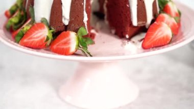 Step by step. Slicing red velvet bundt cake with cream cheese frosting garnished with fresh strawberries.