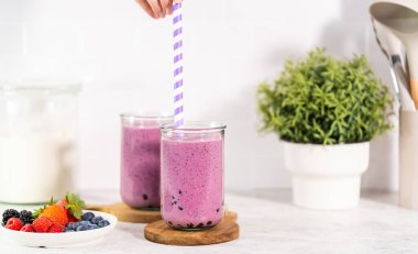 Pouring freshly made mixed berry boba smoothie into a drinking glass.