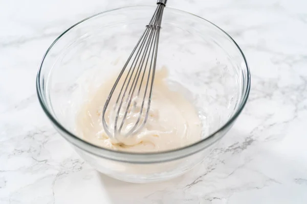 Mixing ingredients with a hand mixer in a large mixing bowl to make the lemon glaze for mini Easter bread kulich.