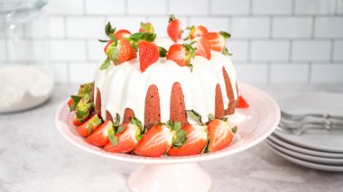 Step by step. Slicing red velvet bundt cake with cream cheese frosting garnished with fresh strawberries.