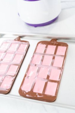 Mini pembe çikolatalar yapmak için silikon çikolata kalıbını erimiş çikolatayla dolduruyorum..