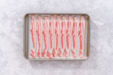 Flat lay. Uncooked bacon strips on a baking sheet with white parchment paper.