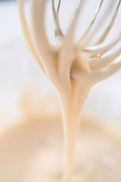 Lemon glaze. Mixing ingredients with a hand whisk in a glass mixing bowl to make lemon glaze.