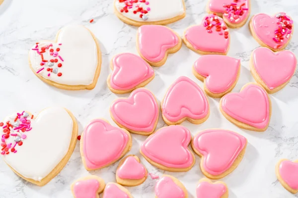 Decorating heart-shaped sugar cookies with pink and white royal icing for Valentines Day.