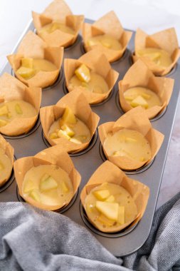 Sharlotka çörekleri pişirmek için parşömen kağıtlarıyla kaplanmış kek tavasına hamur atıyorlar..