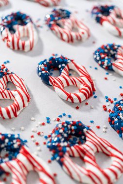 Dipping pretzels twists into melted chocolate to make red, white, and blue chocolate-covered pretzel twists.