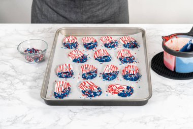 Flat lay. Dipping pretzels twists into melted chocolate to make red, white, and blue chocolate-covered pretzel twists.