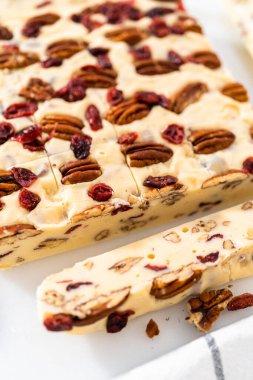 Beyaz çikolatalı fındıklı fındıklı şekerlemeyi beyaz bir kesme tahtasında küçük parçalara ayırmak..