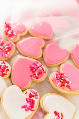 Kalp şeklinde şeker kurabiyelerini büyük plastik bir kapta pembe ve beyaz kraliyet kreması ile depolamak.