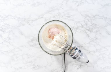 Flat lay. Whisking buttercream frosting in a glass mixing bowl with an electric hand mixer to prepare the peppermint buttercream frosting.