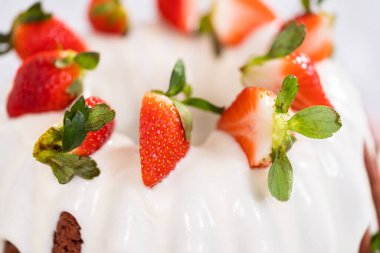 fresh strawberries..Red velvet bundt cake with cream cheese frosting garnished with fresh strawberries on a pink cake stand for Valentines Day.