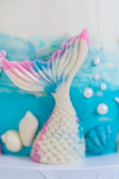 人魚をテーマにした3層のバニラケーキにチョコレートマーメイドの尾と貝殻が白いケーキスタンドに飾られています — ストック写真