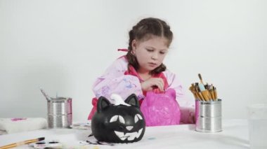 Cadılar Bayramı için akrilik boyayla balkabağı boyayan küçük kız..