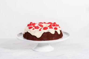 Freshly baked red velvet bundt cake with chocolate lips and hearts over cream cheese glaze for Valentines Day.