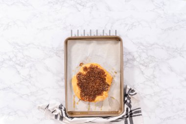 Düz yatıyordu. Parşömen kağıdıyla kaplı bir kabın üzerinde tarçınlı tatlı pizzası hazırlıyorum..