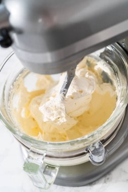 Whisking buttercream frosting in a glass mixing bowl with an electric kitchen mixer for American flag mini cupcakes.