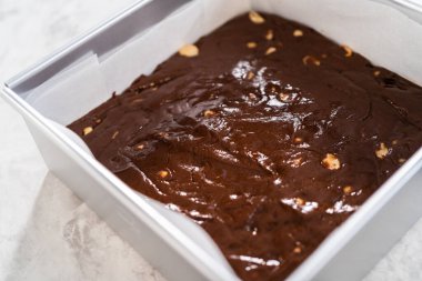 Kare peynirli kek tepsisi çikolatalı macadamia şekerlemesi hazırlamak için parşömen kağıdıyla kaplı..
