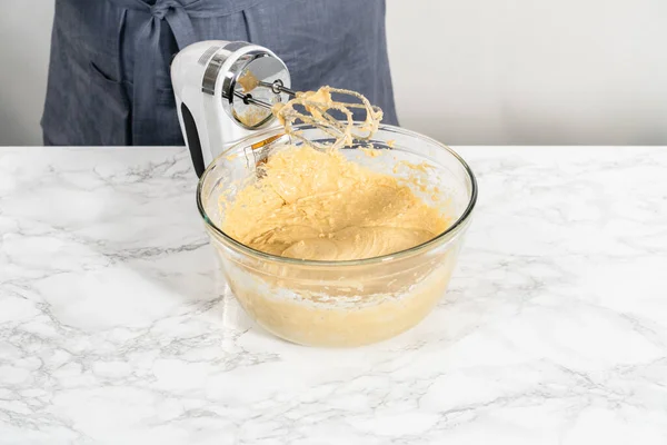 Mixing ingredients with a hand mixer in a large mixing bowl to bake eggnog bundt cake.