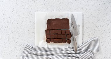 Flat lay. Cutting plain homemade fudge into small pieces on a white cutting board.