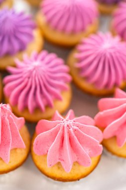 Beyaz pasta standında pembe tereyağlı taze pişmiş mini vanilyalı kekler..