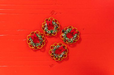 Flat lay. Chocolate pretzel Christmas wreath decorated with sprinkles and red chocolate bow on a red background.