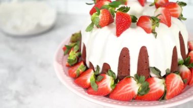 Red velvet bundt cake with cream cheese frosting garnished with fresh strawberries on a pink cake stand for Valentines Day.