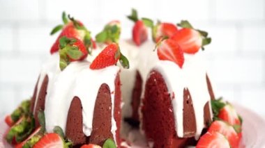 Step by step. Slicing red velvet bundt cake with cream cheese frosting garnished with fresh strawberries.