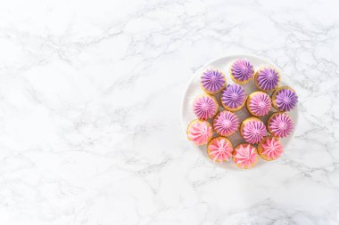 Düz yatıyordu. Beyaz pasta standında pembe tereyağlı taze pişmiş mini vanilyalı kekler..