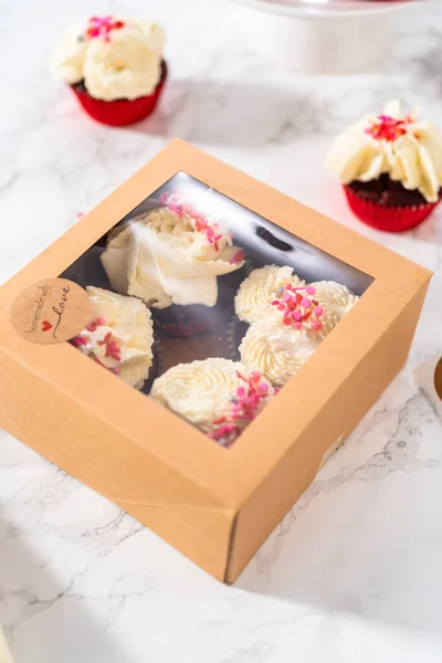 将新鲜烘焙过的红绒纸杯蛋糕与白巧克力软糖糖霜一起装入纸杯蛋糕盒 — 图库照片